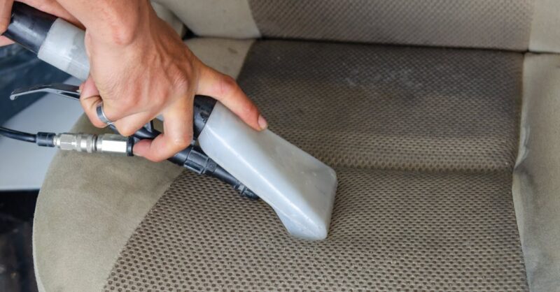 Mão segurando equipamento de limpeza em estofado de carro