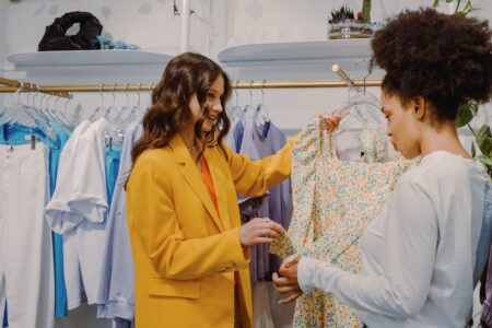 Como o marketing sensorial influencia as suas vendas Cliente sente o tecido de um vestido florido em uma loja de roupas iluminada, exemplo de experiência sensorial no varejo