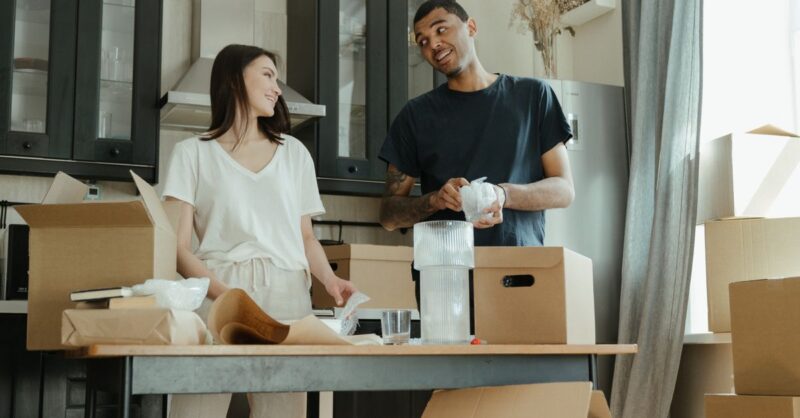 Um homem e uma mulher sorrindo enquanto organizam caixas em uma mesa de trabalho.