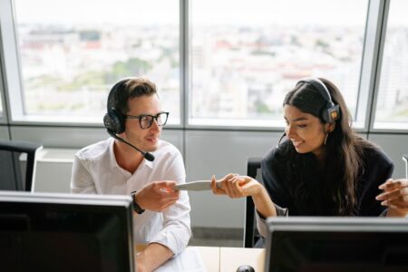 Geração de leads B2B é o maior desafio para 39,1% das empresas brasileiras Dois profissionais de vendas com headset trocam informações de um contato em escritório com vista para a cidade